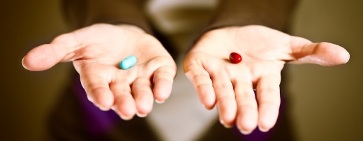 Auf zwei ausgestreckten Händen mit den Handflächen nach oben werden jeweils eine rote und eine blaue Pille angeboten