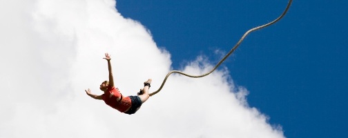 Junge Frau vor Wolken an einem Bungeseil mit ausgestreckten Armen