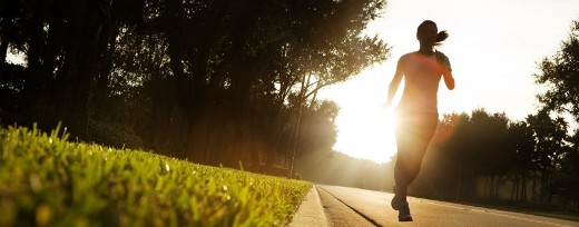 Frau joggt früh am Morgen auf der Straße mit der tief stehenden Sonne im Hintergrund