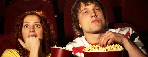 Mann und Frau sitzen im Kino. Sie zeigt Angst, er sitzt ungerührt da und isst Popcorn.