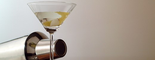 Martini-Glas mit Olive und Cocktail-Shaker im Hintergrund
