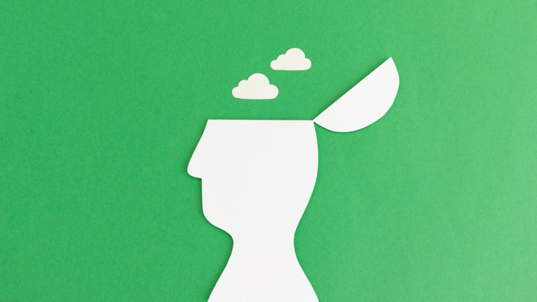 Weiße Papier-Silhouette von einem Kopf mit aufgekappter Schädeldecke aus dem Wolken aufsteigen vor grünem Hintergrund