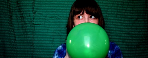 Junge Frau pustet grünen Luftballon auf