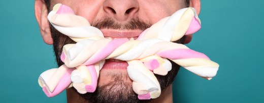 Mann beißt auf mehrere bunte Zuckerstangen aus Schaum