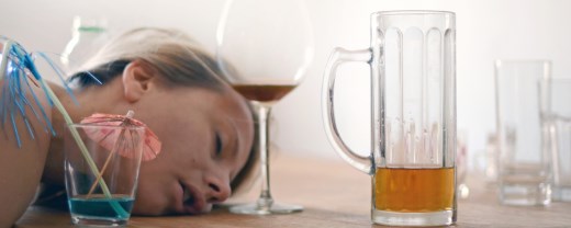 Frau liegt mit Kopf auf Tisch vor halbleeren Alkoholgläsern