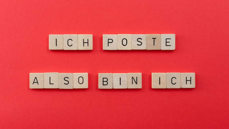 Text "Ich poste, also bin ich" mit Scrabble-Buchstaben vor rotem Hintergrund