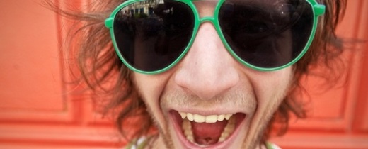 Junger Mann mit großer Sonnenbrille mit grünem Rand lacht