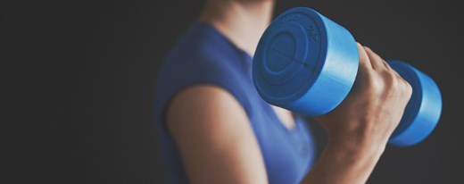 Frau mit blauer Hantel (2 kg) vor dunklem Hintergrund