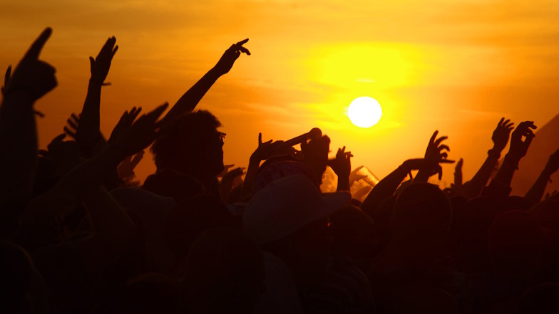 Gegenlichtaufnahme einer tanzenden Menge mit Armen in der Luft auf einem Festival