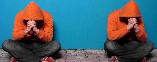 Zwei Personen mit orangen Kapuzenpullis im Schneidersitz vor blauer Wand