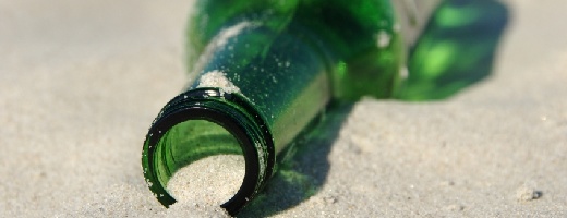 Leere Bierflasche liegt im Sand, halb mit Sand gefüllt