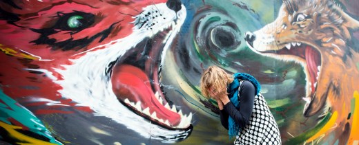 Frau steht mit Händen vor dem Gesicht vor Wand mit aufgemalten Füchse, die ihr Maul aufreißen