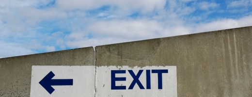 Betonwand mit Aufschrift Exit und Pfeil nach links, darüber blauber Himmel mit leichter Bewölkung