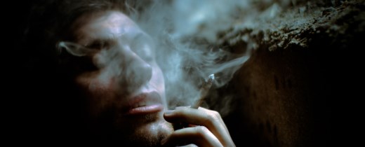 Junger Mann raucht einen Joint mit geschlossenen Augen, Rauch steigt auf