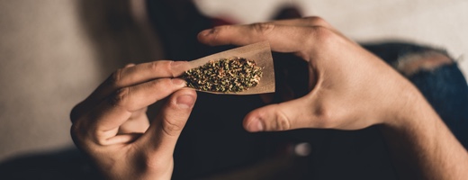 Zwei Hände halten Zigarettenpapier gefült mit Cannabis und Tabak