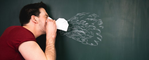 Mann niest in Taschentuch vor Tafel mit aufgemalten Tropfen