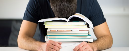 Junger Mann lässt seinen Kopf auf einem Stapel Bücher hängen