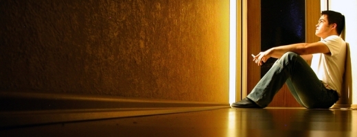 Mann sitzt in einem leeren Raum auf dem Boden und raucht, eine Tür dahinter steht einen Spalt offen Mann sitzt in einem leeren Raum auf dem Boden und raucht, eine Tür dahinter steht einen Spalt offen
